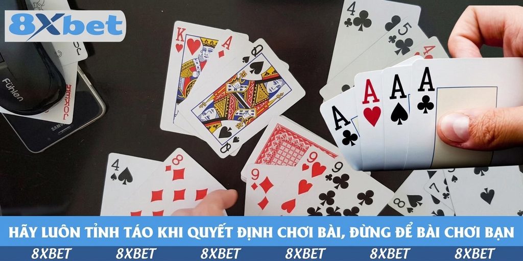 Nhiều lá bài Tây gồm K cơ, Q bích, 9 cơ, 8 rô, 4 cơ nằm rải rác trên mặt bàn tối cạnh chiếc điện thoại