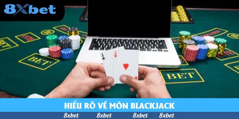Áp dụng chiến thuật Blackjack online: tay người chơi cầm hai lá Át và một lá cơ trước laptop, xung quanh là chồng phỉnh trên bàn Blackjack có ô BET
