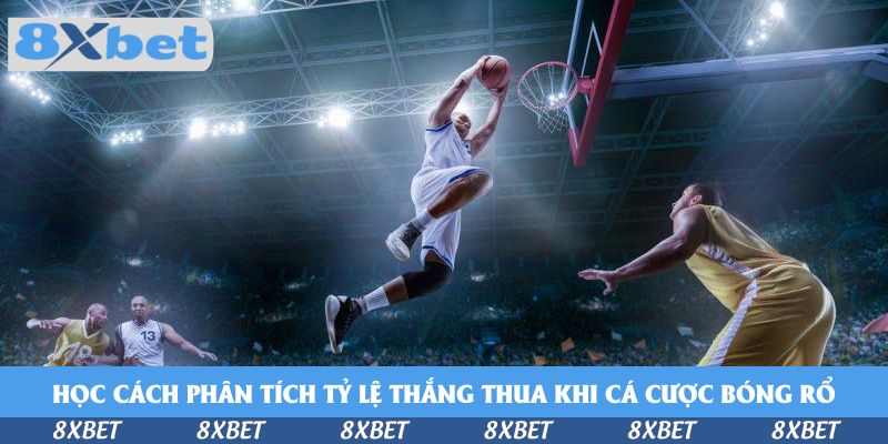 Cầu thủ áo trắng bật nhảy úp rổ trong nhà thi đấu sáng đèn trước hậu vệ áo vàng