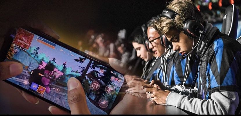 Minh họa esports là gì: tay cầm điện thoại chơi game bắn súng bên cạnh hàng tuyển thủ đeo tai nghe đang thi đấu