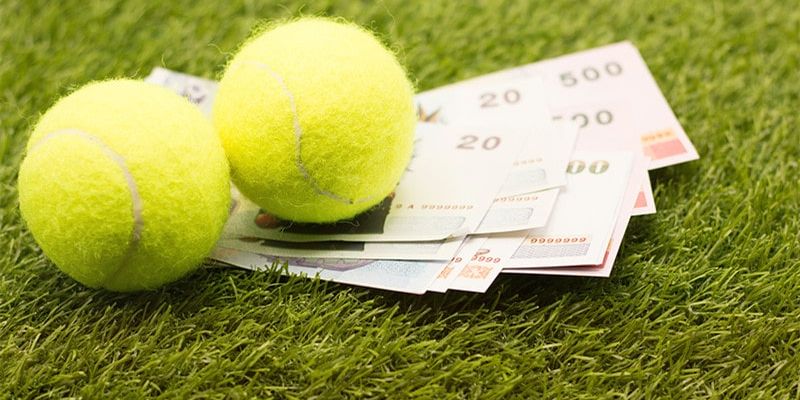 Hai quả bóng tennis màu vàng xanh đặt trên xấp tiền giấy trên thảm cỏ